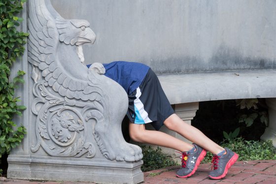 A young child bent over at the end of a stone bench.